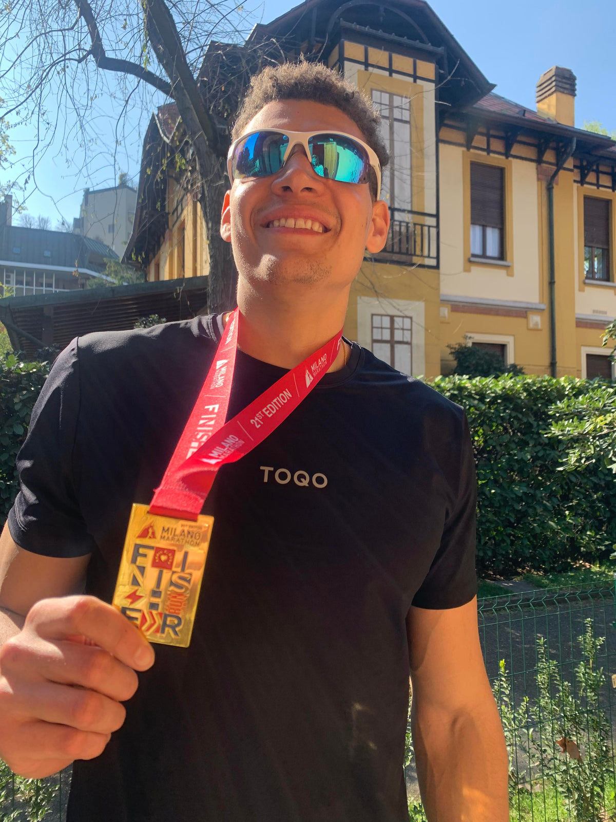 A man holding a medal in front of a house.